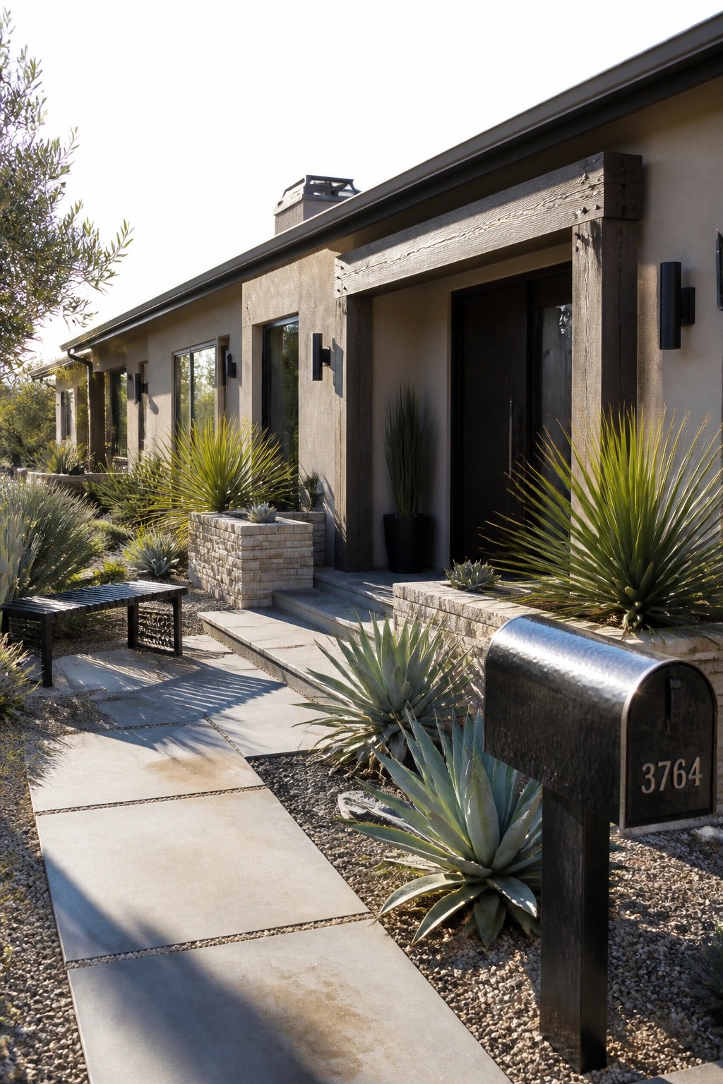 A long low ranch home with beige stucco walls, dark wood trim around the entry, a black front door, stone steps, and desert plants along a concrete walkway.