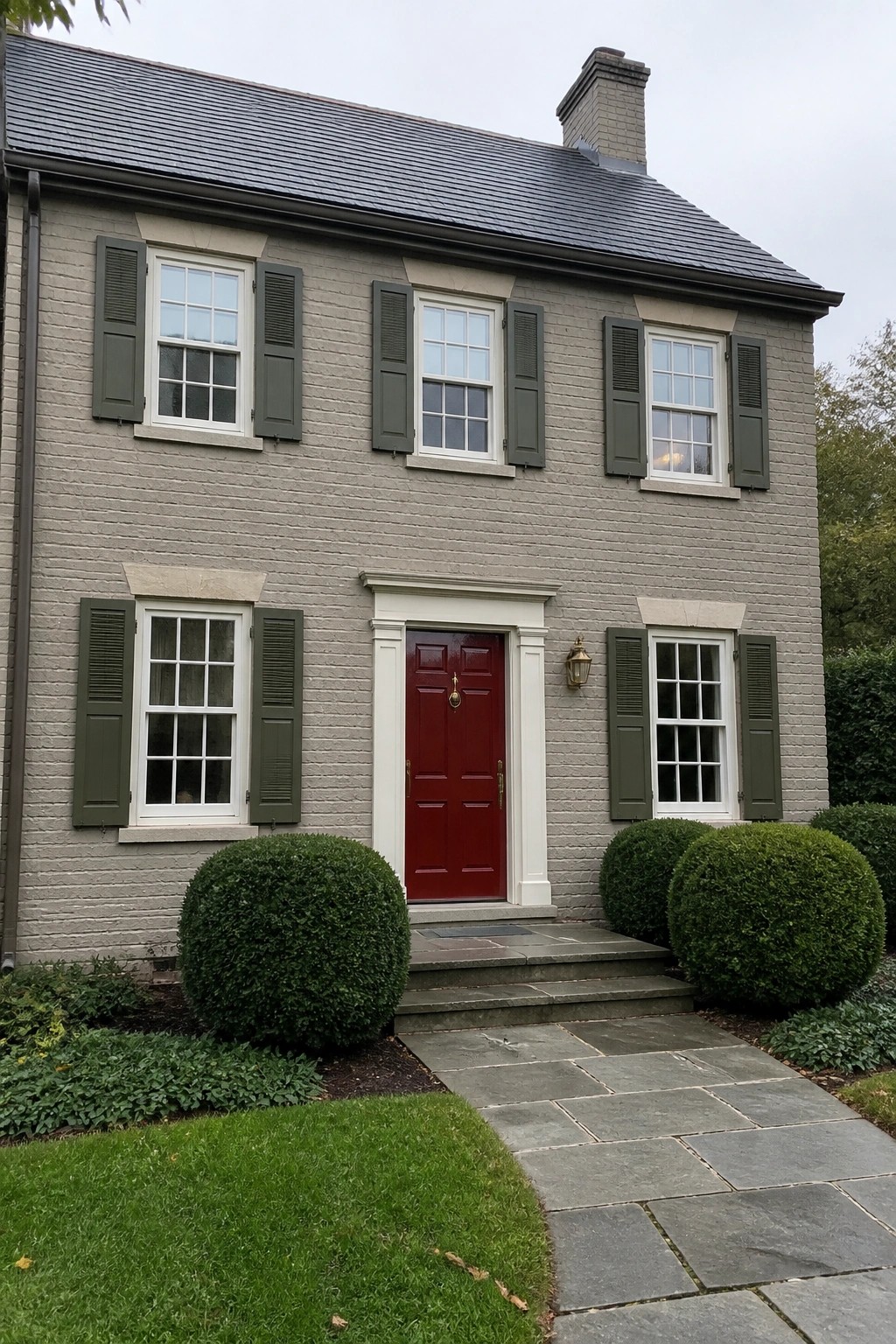 Gray brick two-story house with red door, green shutters, and stone path