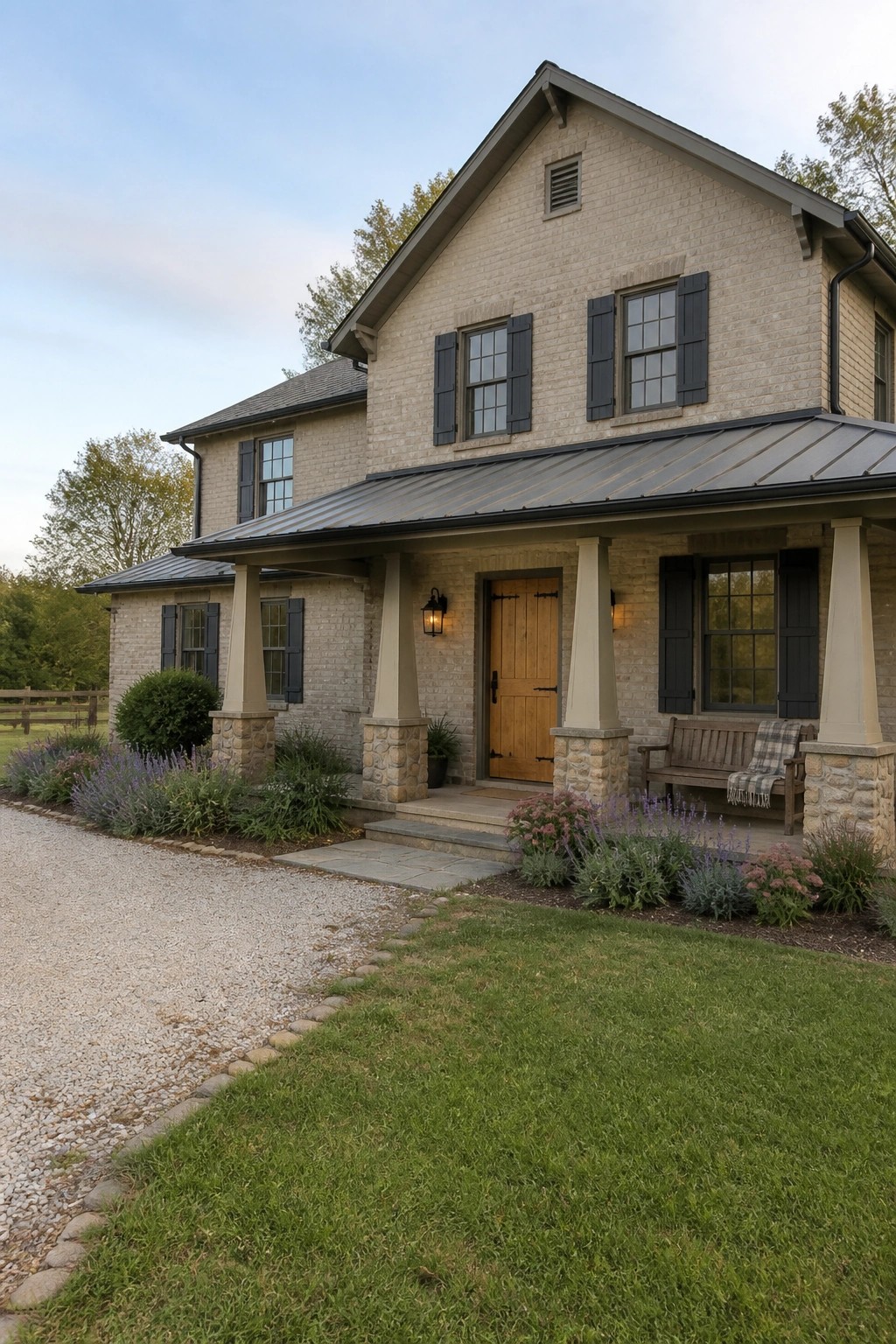 Two-story beige brick house with black shutters, wooden door, and flower-lined porch.