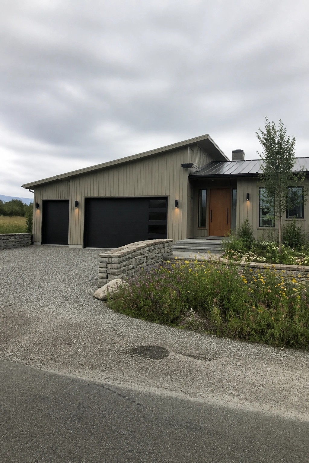 A modern house with muted greige siding and stone accents in a rural setting.