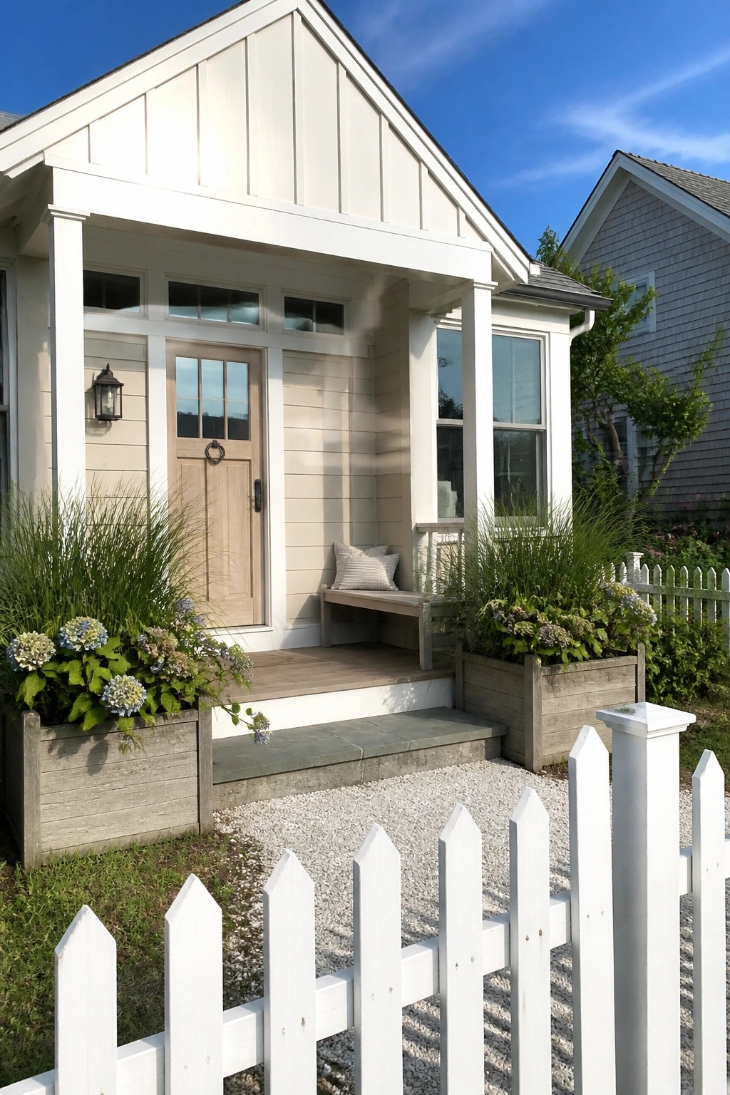 Front view of a small light beige house with a wooden door, covered porch, and wooden planters beside the steps.