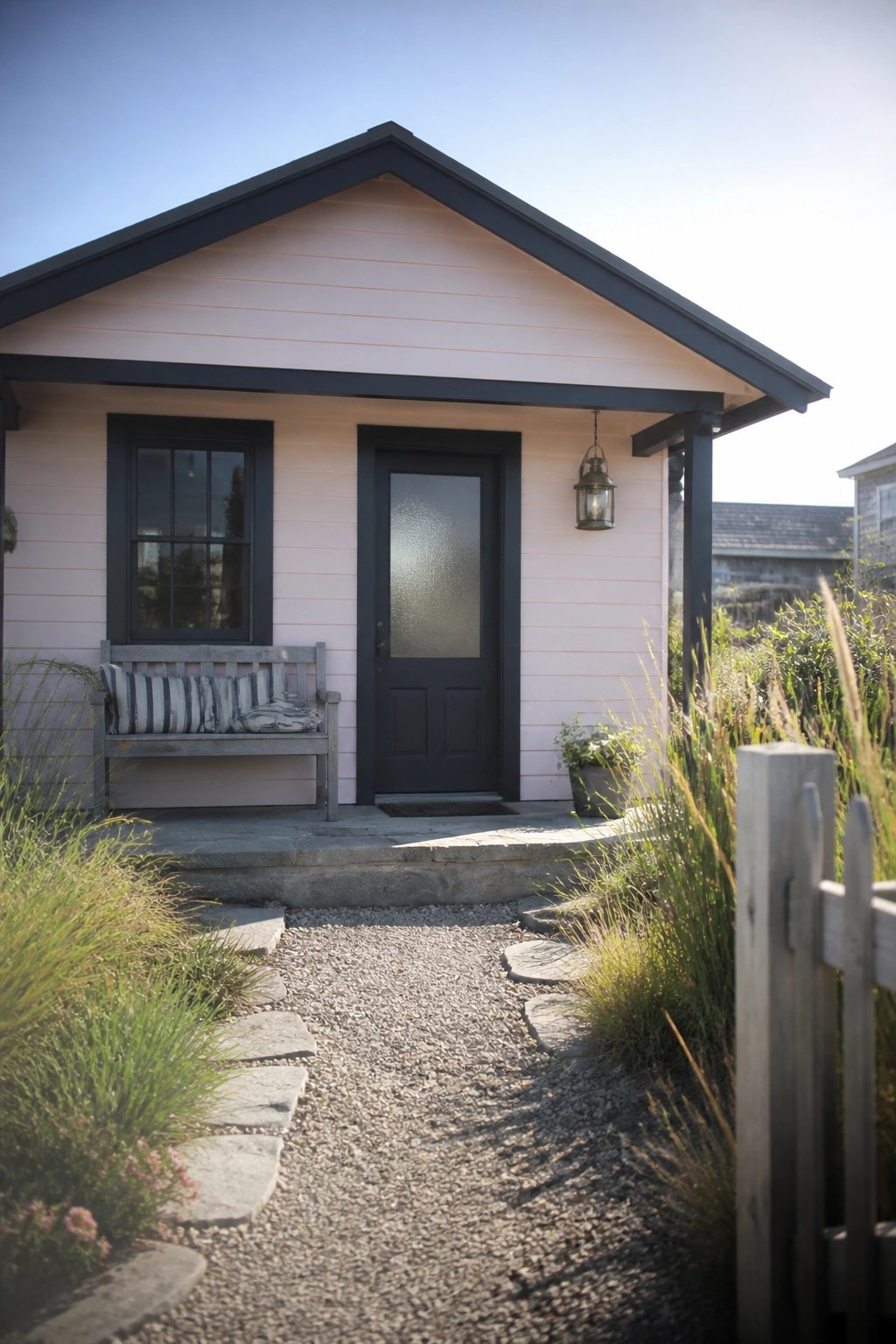 Pink cottage with black door, bench, and gravel stepping-stone path.