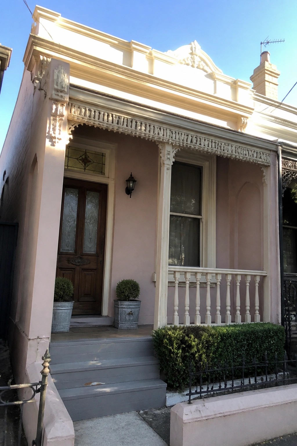 A small light pink house exterior with white trim, a wooden front door with stained glass, gray steps, and a small porch with a white railing.