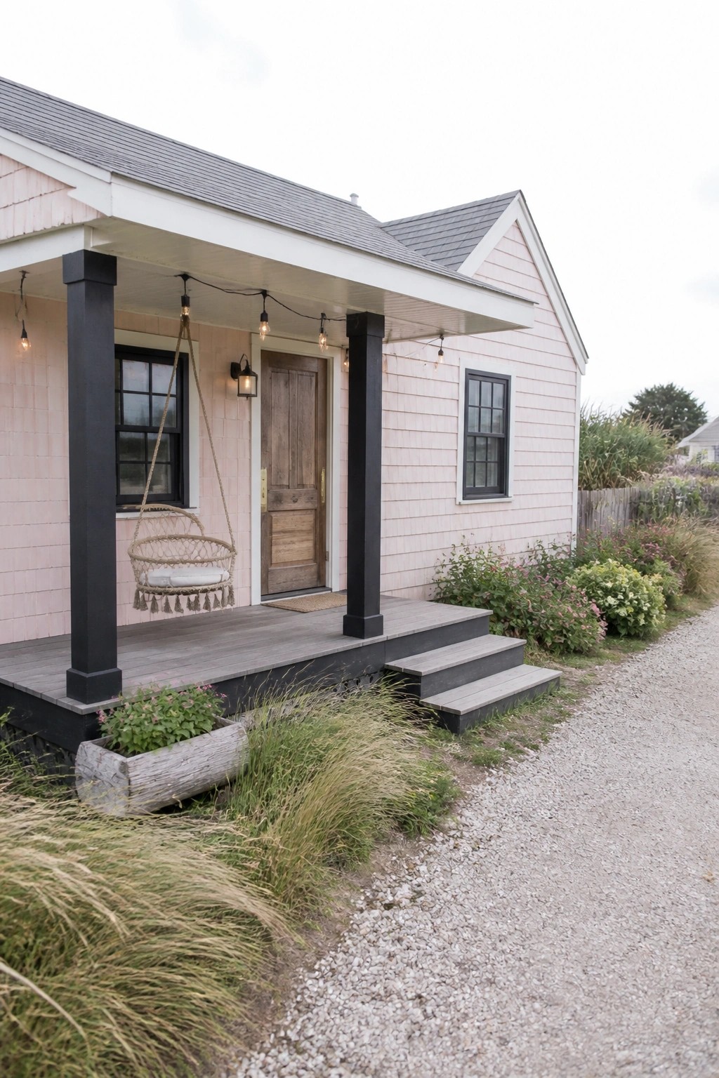 A small house with light pink siding, black porch posts, a wooden front door, and a hanging chair on the porch.