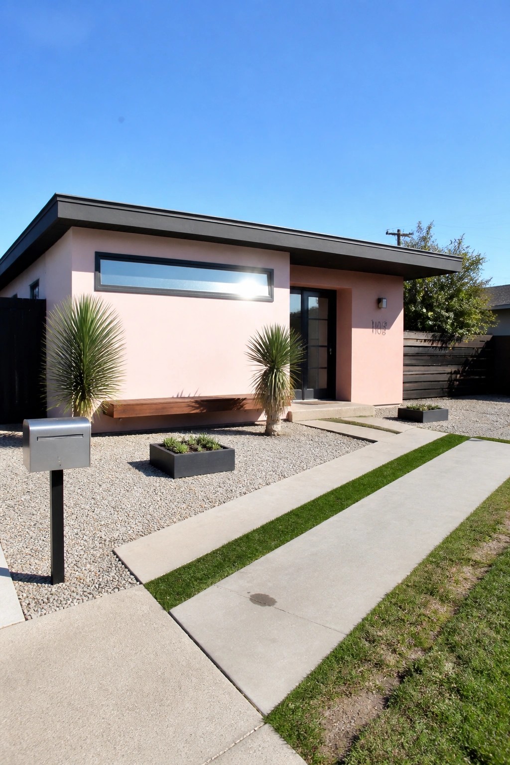 Modern pink house with black roof, concrete path, and gravel garden.