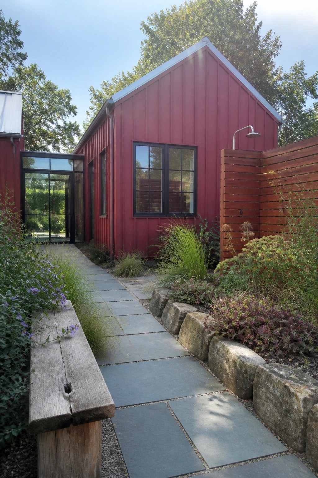 Red building with stone path, wooden bench, garden plants and outdoor shower.