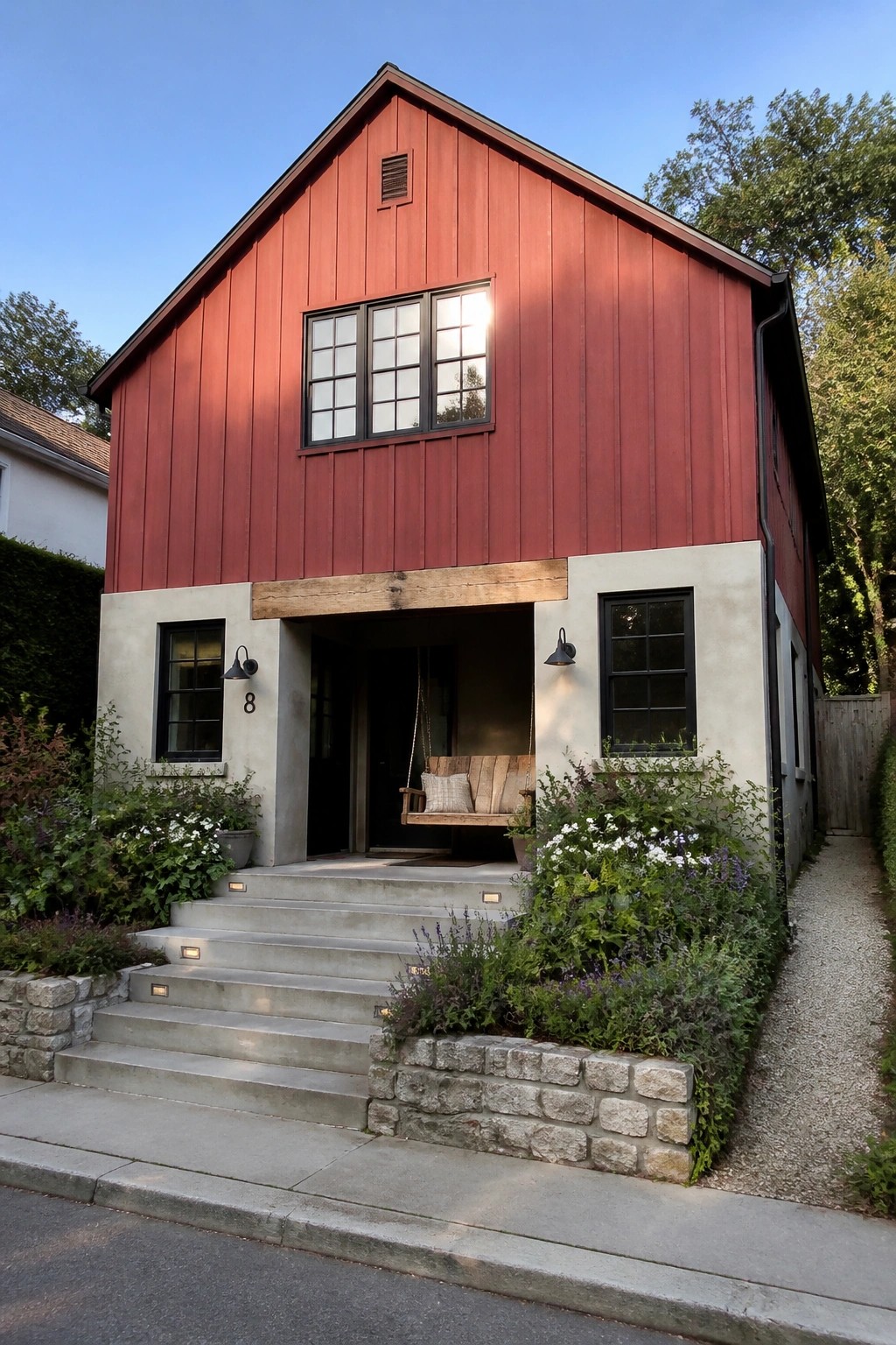 A two-story red barn-style house with vertical wood siding above a concrete lower section, a timber beam over the entry, and a hanging porch swing.