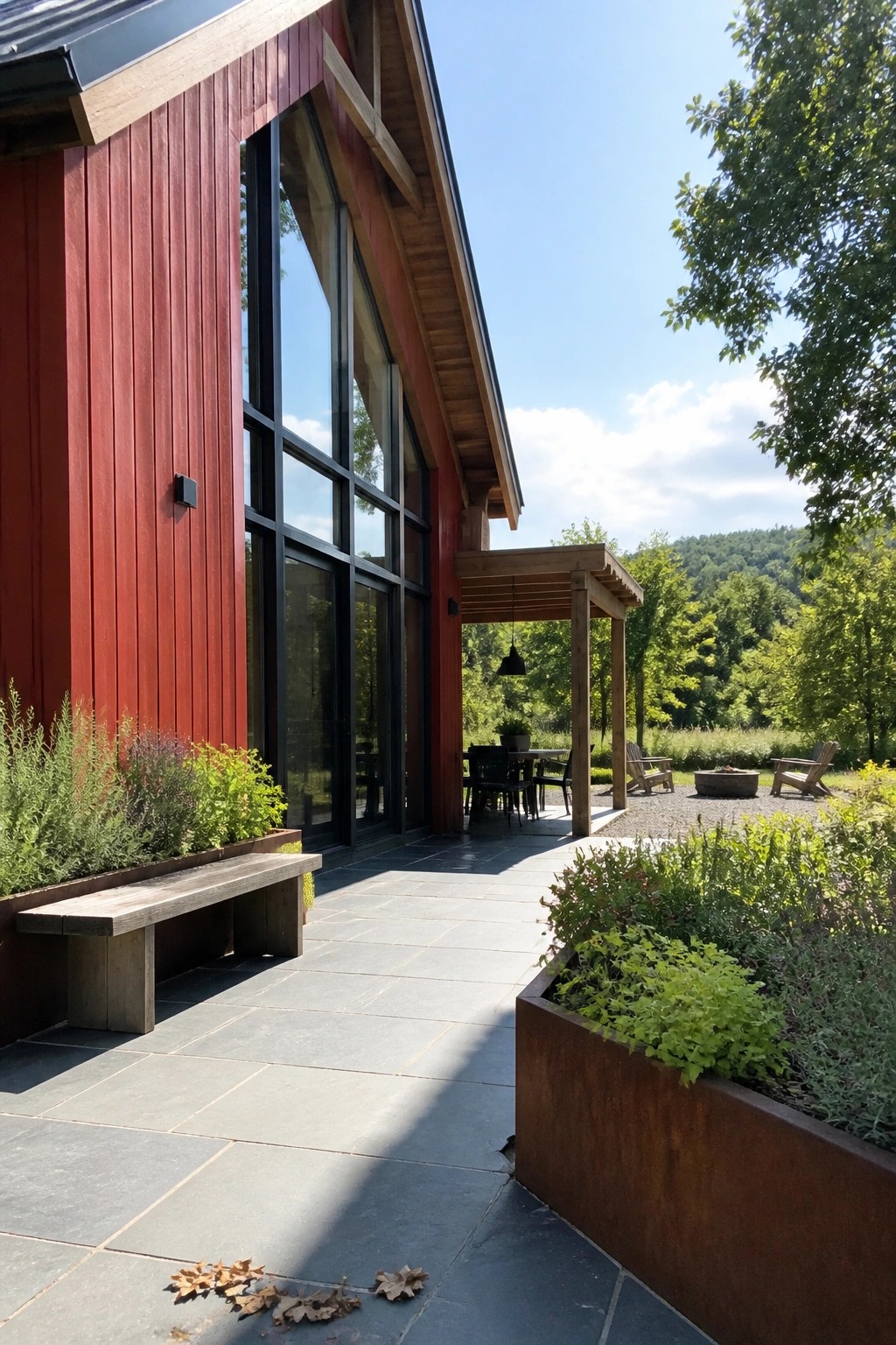 Modern red wooden house with large windows on stone patio amid trees and garden.