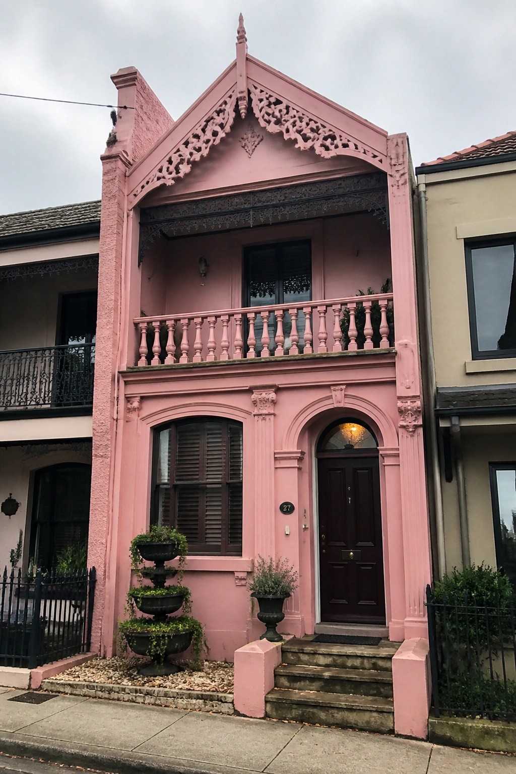 A narrow pink Victorian house with ornate trim, a dark wooden door under an arch, and a small balcony on the second floor.