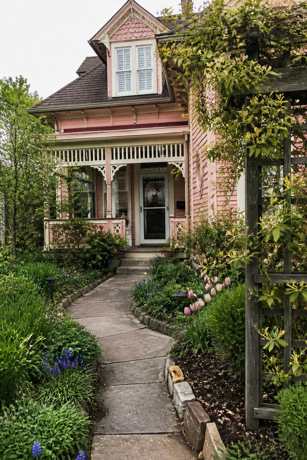 Curving stone path leads through vibrant garden to ornate pink house porch