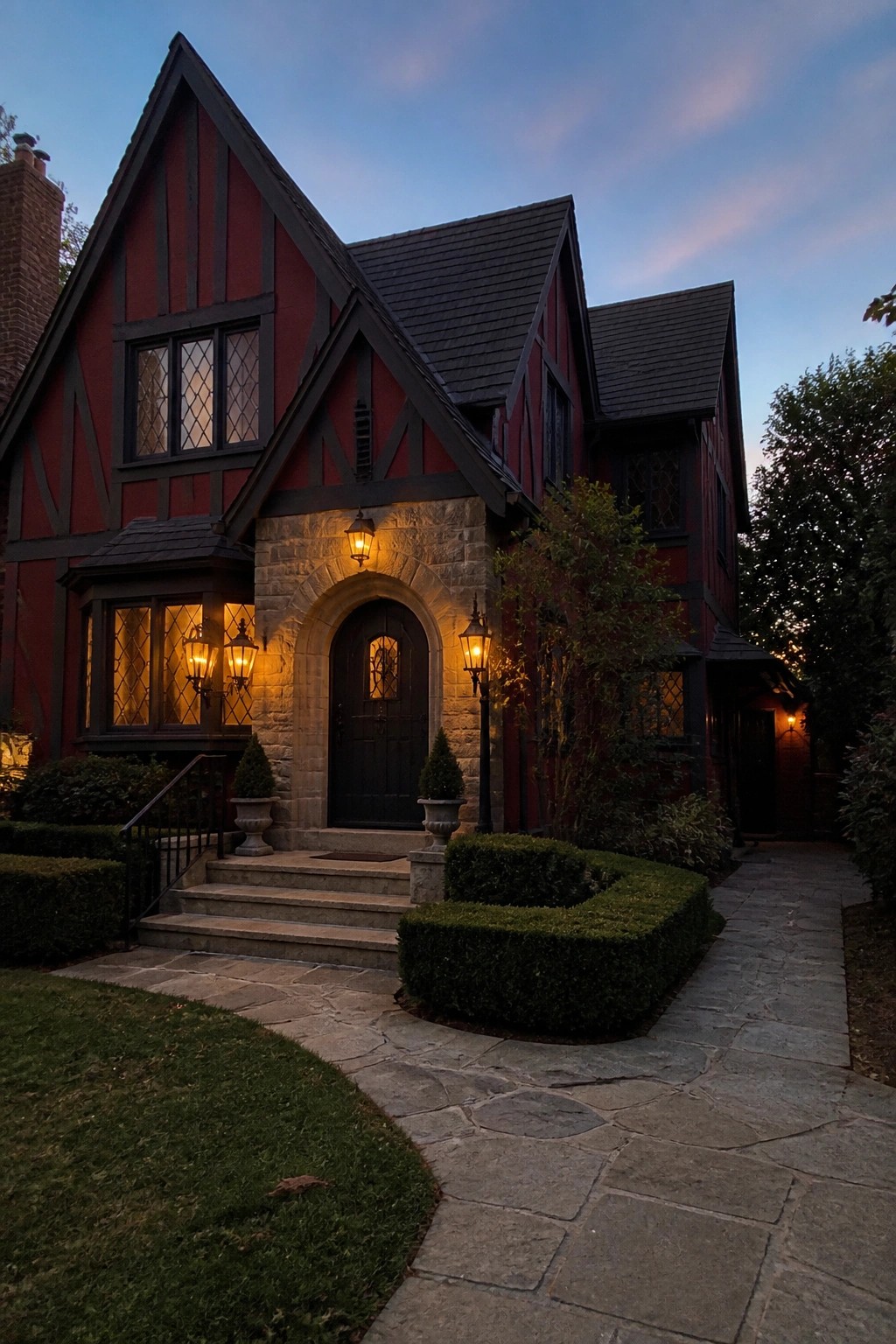 Red Tudor house with stone archway, lit lanterns, and stone path at dusk
