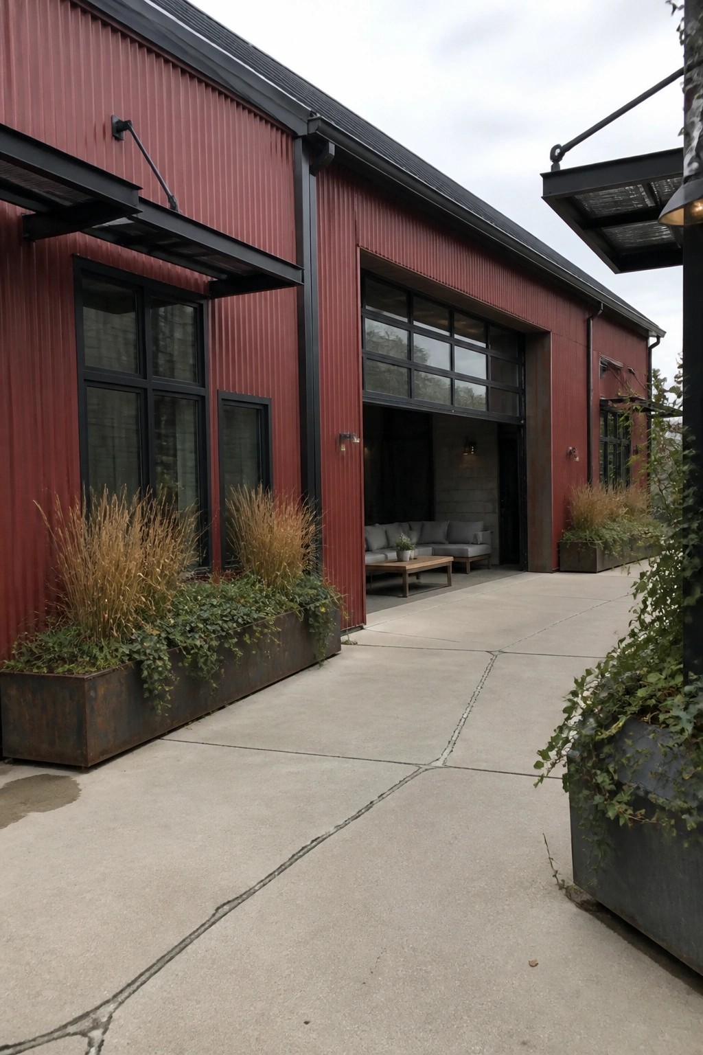 Red corrugated metal building with black windows, open door, and metal planters with grasses