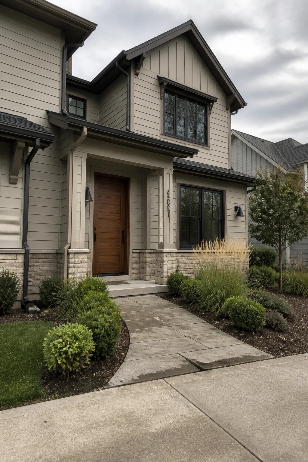 Modern beige house with wooden door, stone porch, black windows, and landscaped walkway.