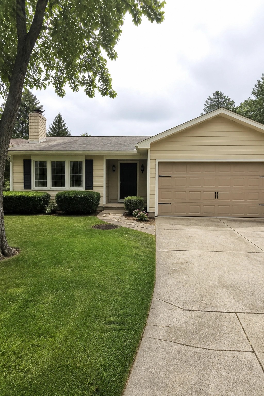 Beige single-story house with attached garage, green lawn, stone path, and driveway.