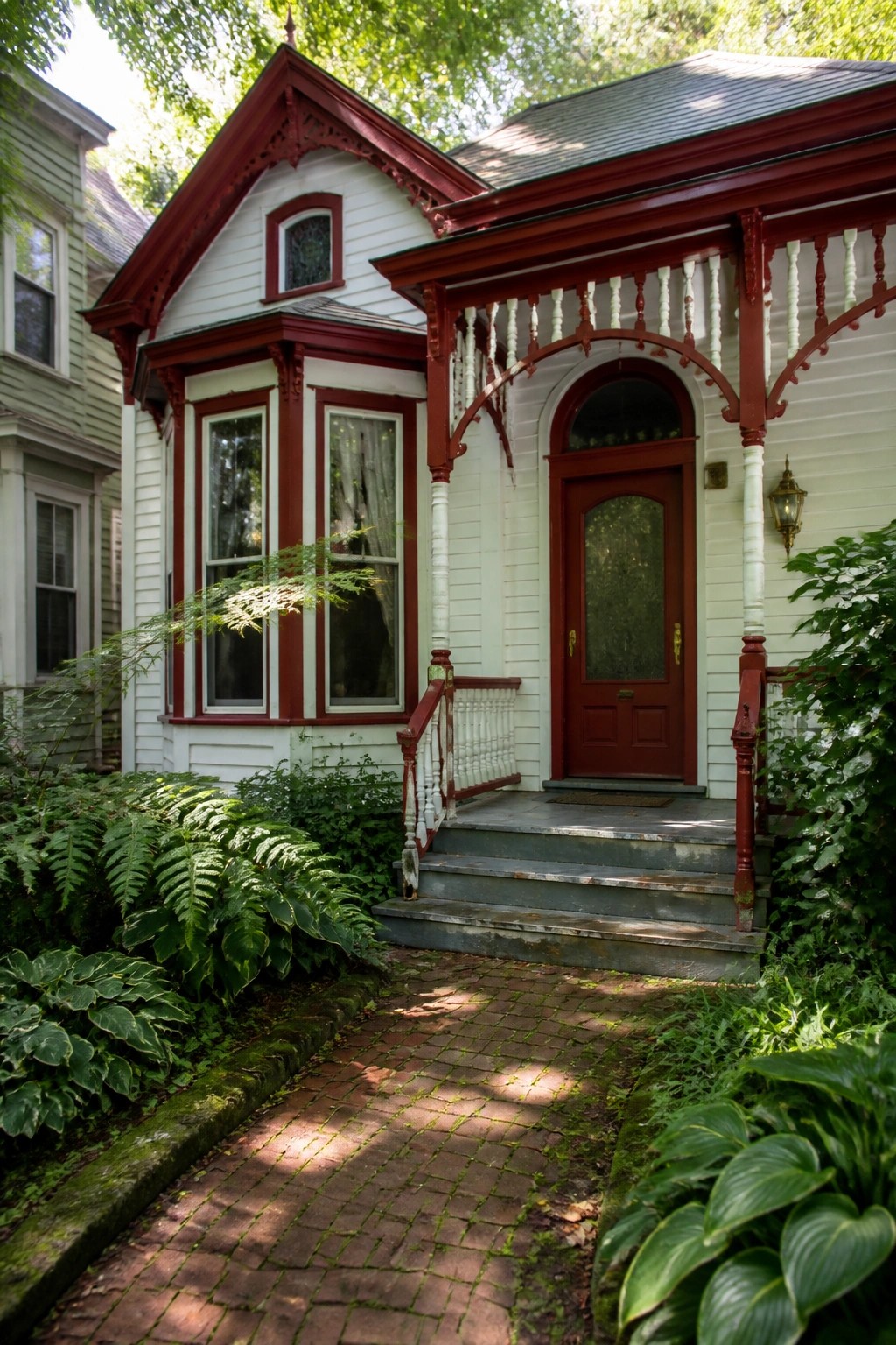 A white house with red trim, a red front door, gray steps, and a brick path lined with green plants.