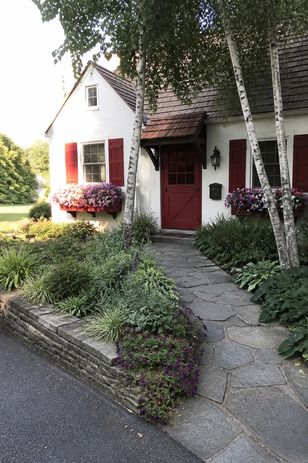 A white house exterior with a red door, red shutters, and flower boxes beside a stone path.