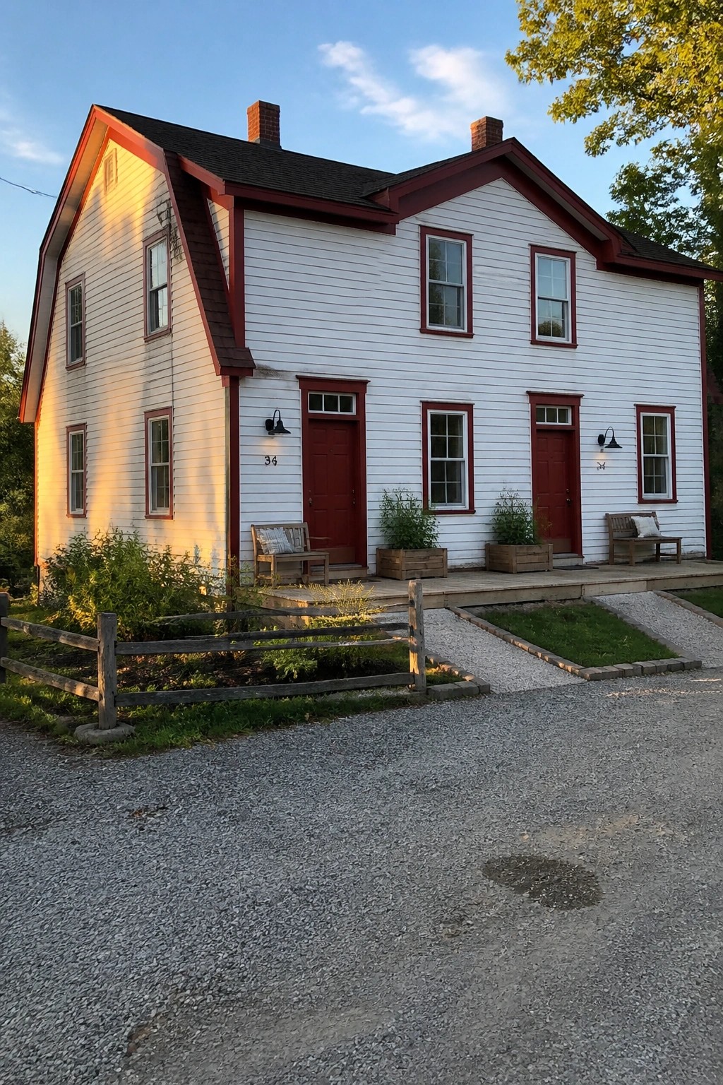 White two-story house with red trim, dual red doors, porch benches and gravel drive.
