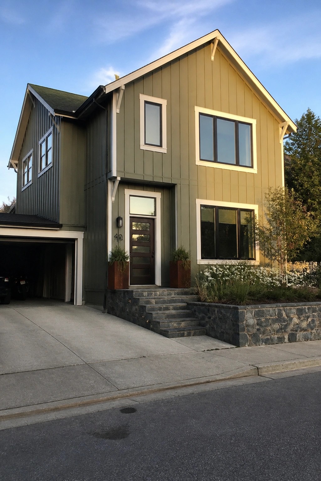 Modern two-story sage green house with white trim, large windows, and stone steps