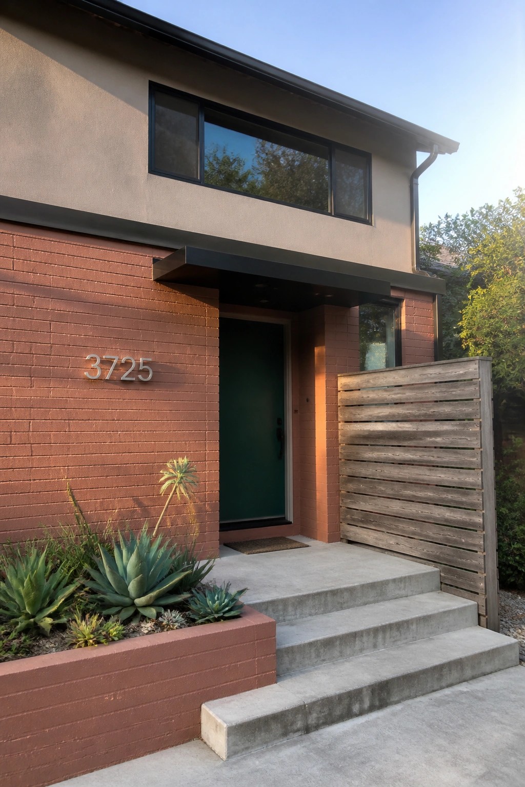 Modern home exterior with warm terracotta brick siding, concrete steps, and a dark green door.