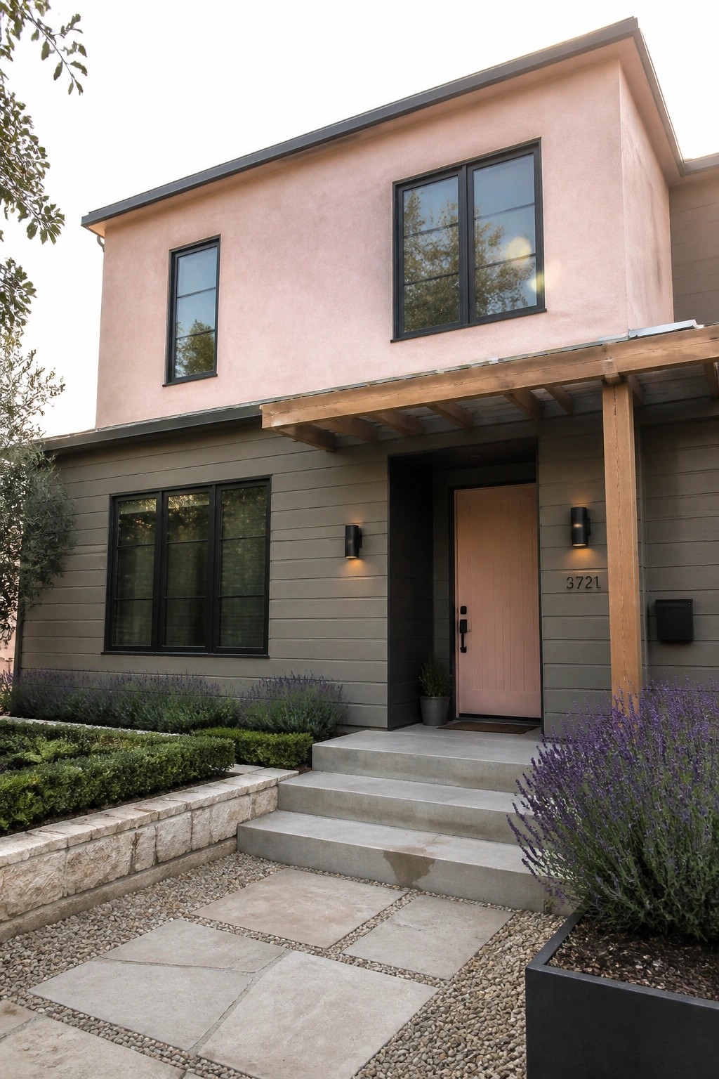 A two-story contemporary house with pink stucco on the upper level, gray siding below, black-framed windows, a pink front door, and concrete steps leading to the entry.