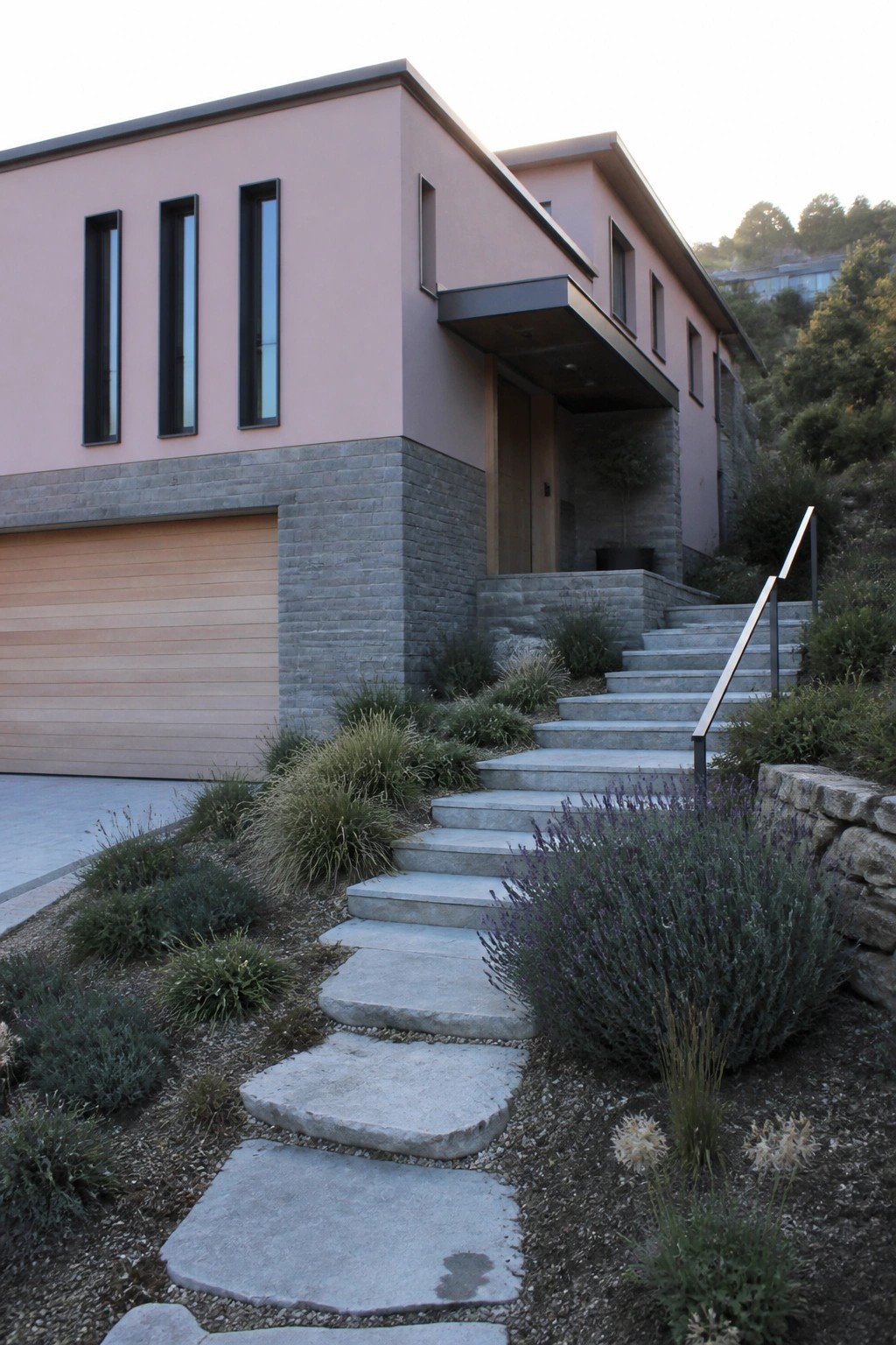 Modern pink house with wooden garage, stone steps, and lavender landscaping.