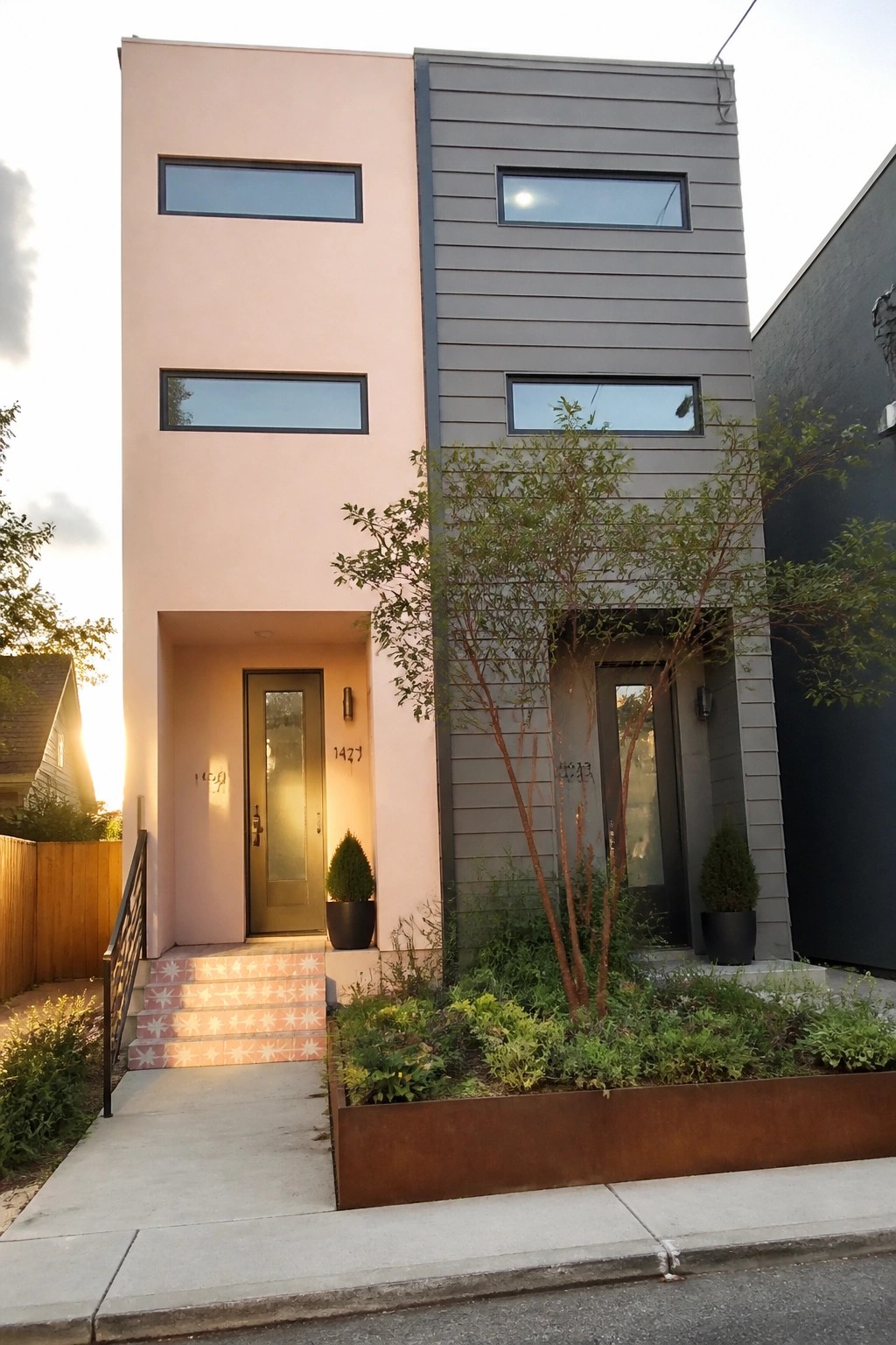 A modern two-story duplex with a pink stucco left half and gray siding right half, each with its own front door and horizontal windows.