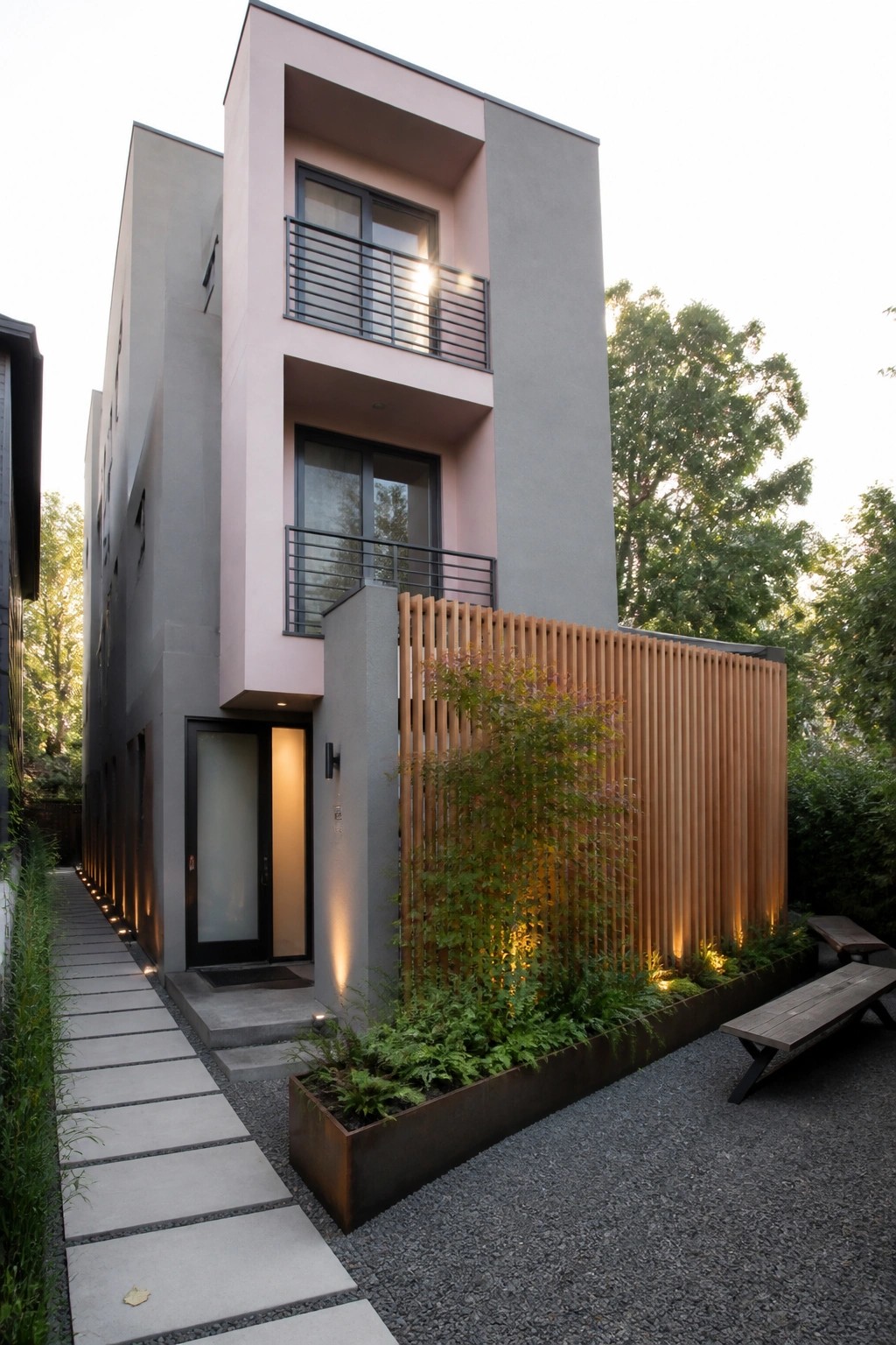 Modern pink-gray building with balconies, vertical wood screen, gravel patio and benches