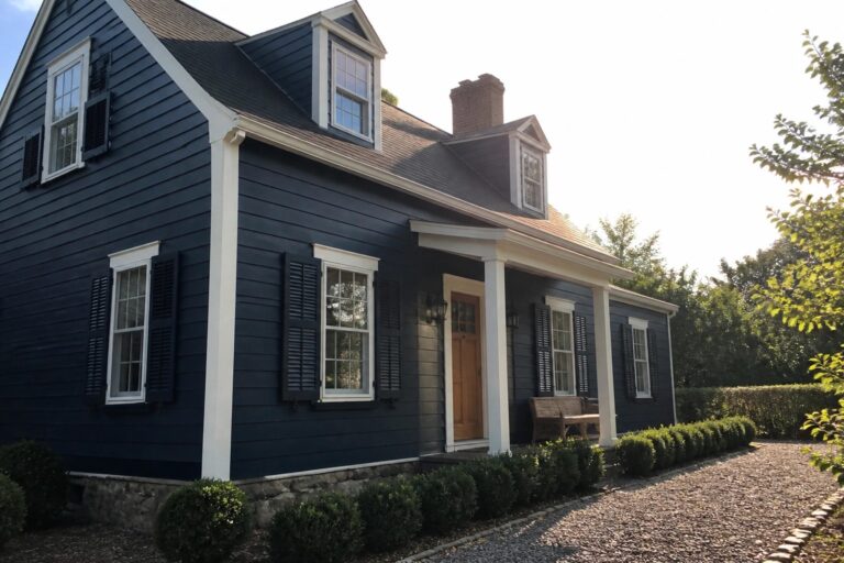 Dark blue house with white porch columns, black shutters, and gravel path