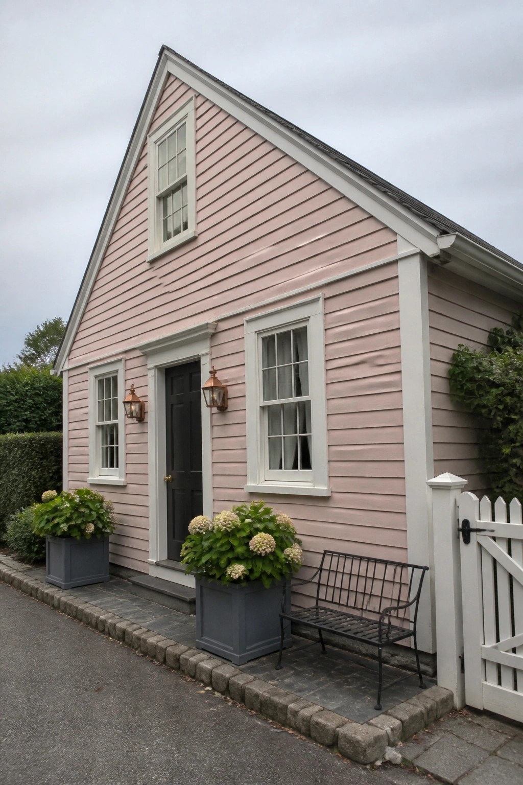 Pink house with white trim, dark door, potted hydrangeas, black bench, white gate.