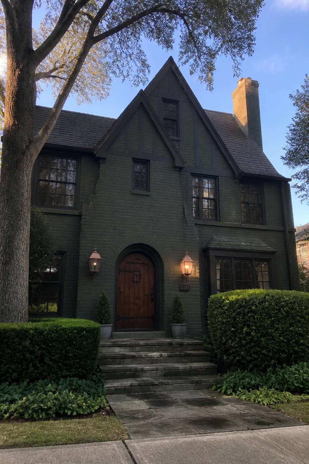 A large two-story house painted deep dark green with brick accents around the arched entry.