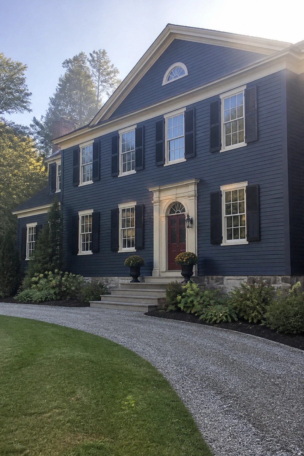 Two-story dark blue house with white trim, black shutters, and red door