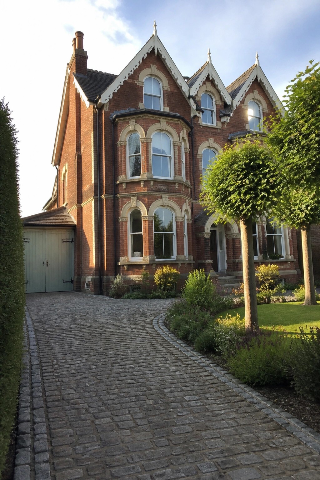 Ornate red-brick Victorian house with bay windows and cobblestone driveway.