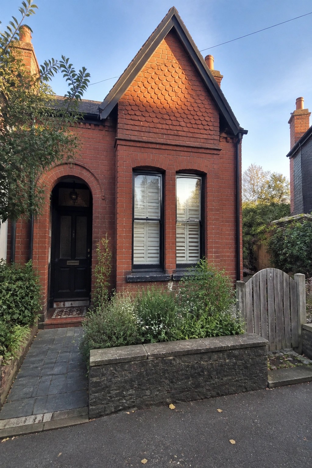 Red brick house with arched black door, shuttered windows, and garden.