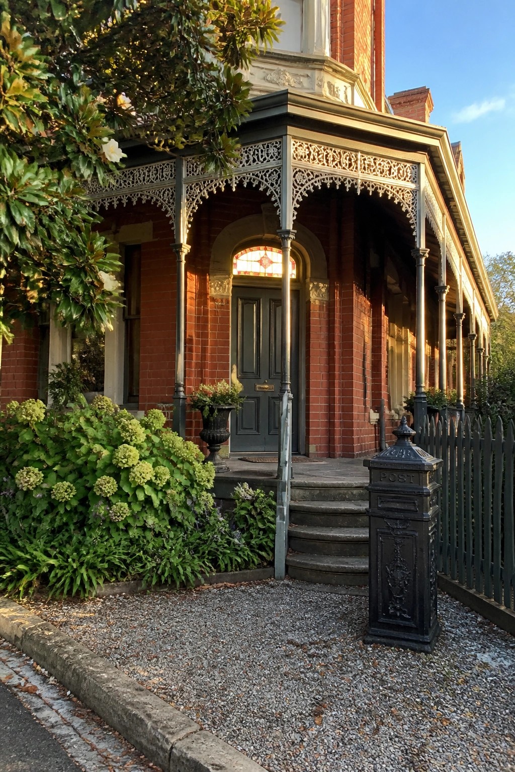 Red brick Victorian house with ornate porch, dark door, steps, and black postbox