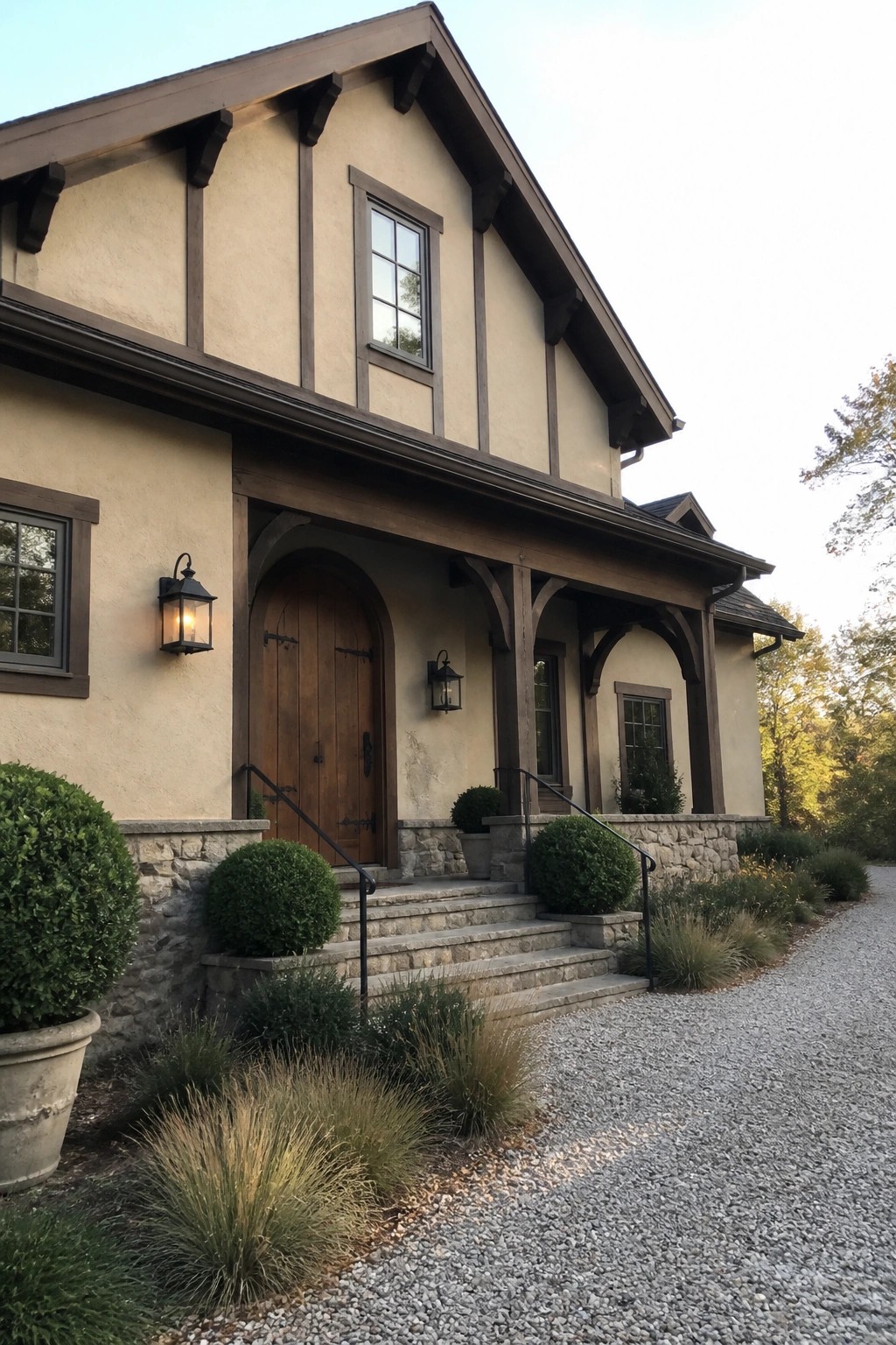 A two-story house with beige stucco walls, dark wood trim and beams, an arched wooden front door, and a stone base along the entry steps.