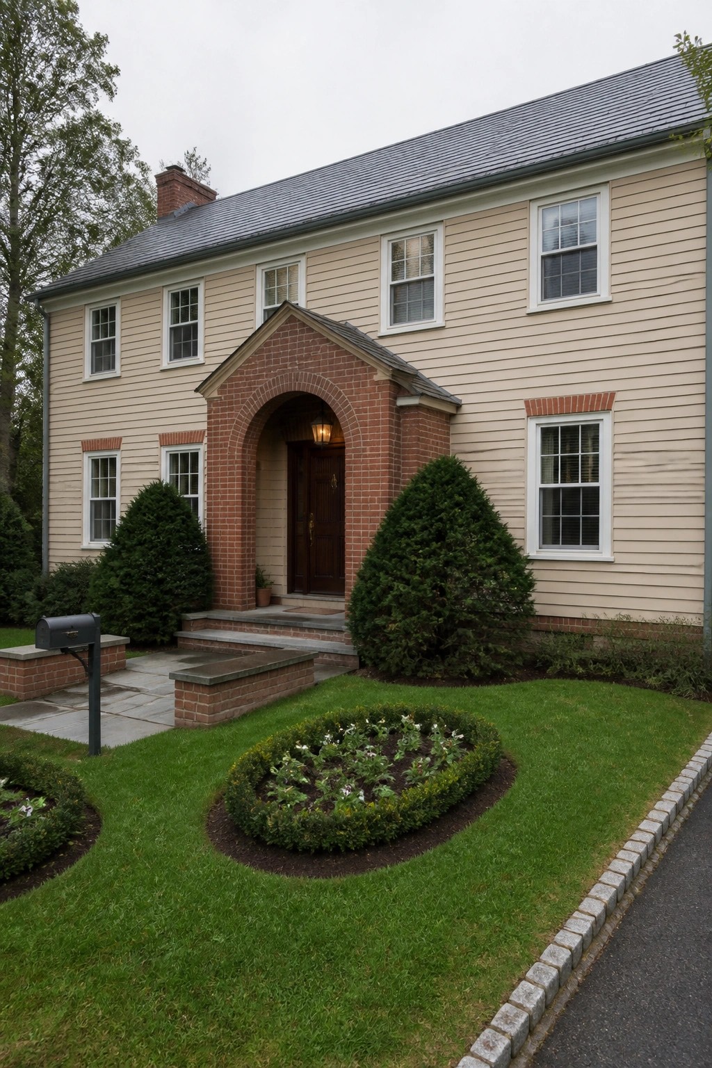 A two-story beige house with red brick details framing the front door in an arch, plus brick trim on several windows and a curved garden bed in the foreground.
