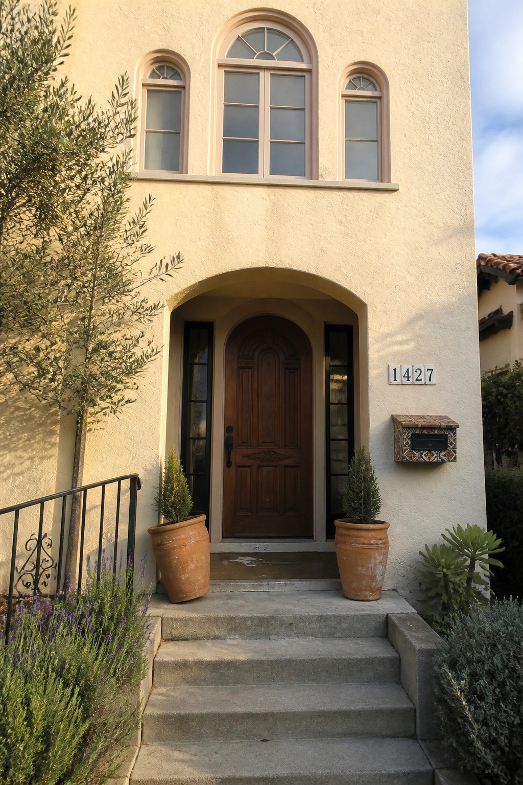 Beige stucco house with arched wooden door, steps, and terracotta pots.