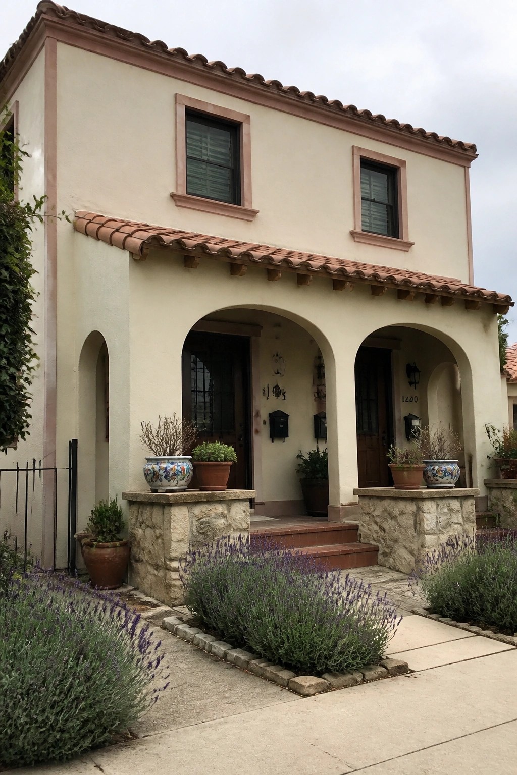 Beige stucco house with arched porch, terracotta roof, stone pillars, and lavender garden.
