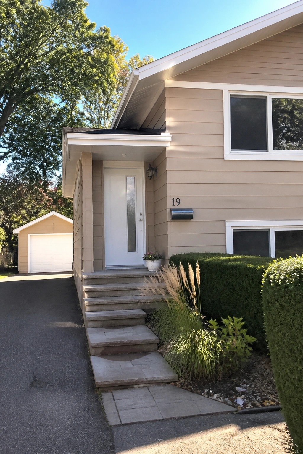 Beige house exterior with white trim around the front door and windows, concrete steps, and a small garden bed beside the entrance.