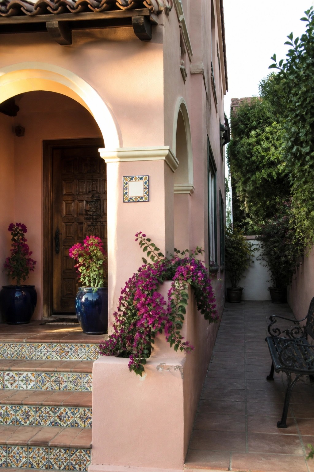 Pink stucco villa with arched doorway, tiled steps, and magenta bougainvillea.