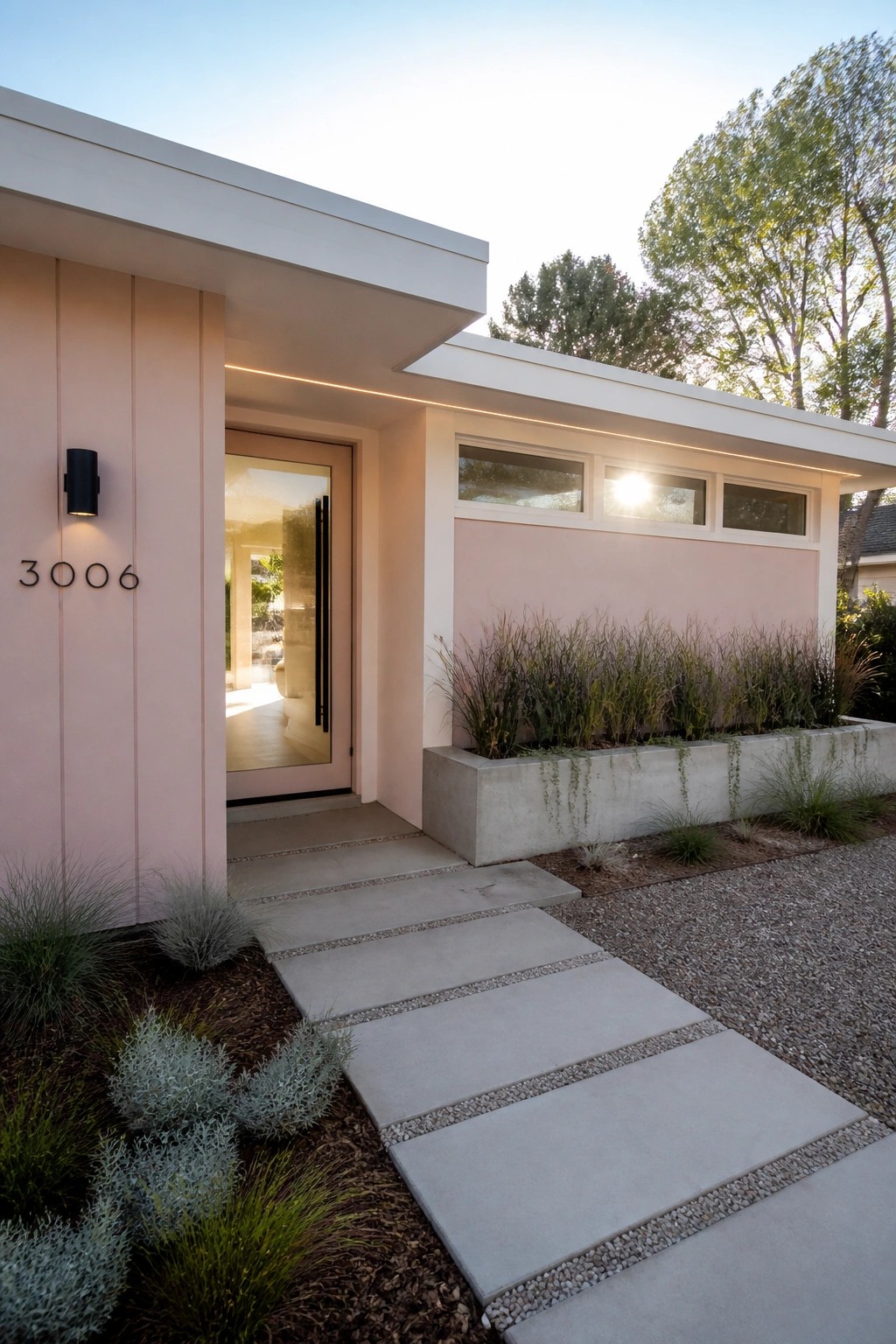 Modern pink house entrance with open door, concrete steps, and gravel garden path
