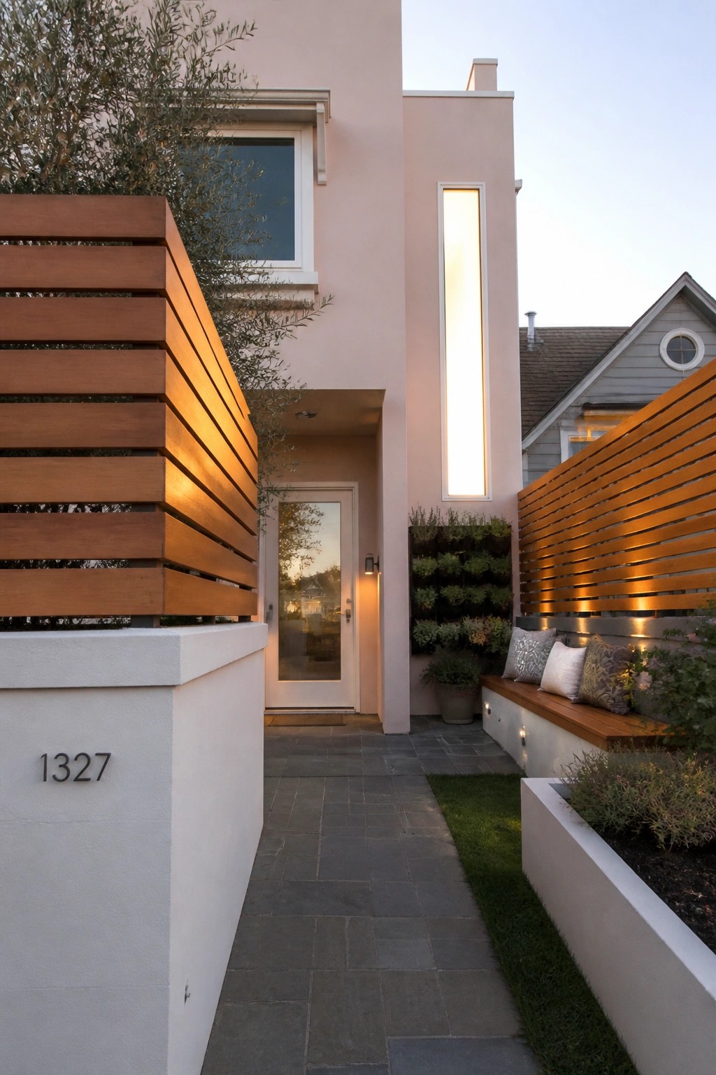 A blush pink house exterior with white trim around the door and window, a paved stone walkway, and horizontal wood slats on the side wall.