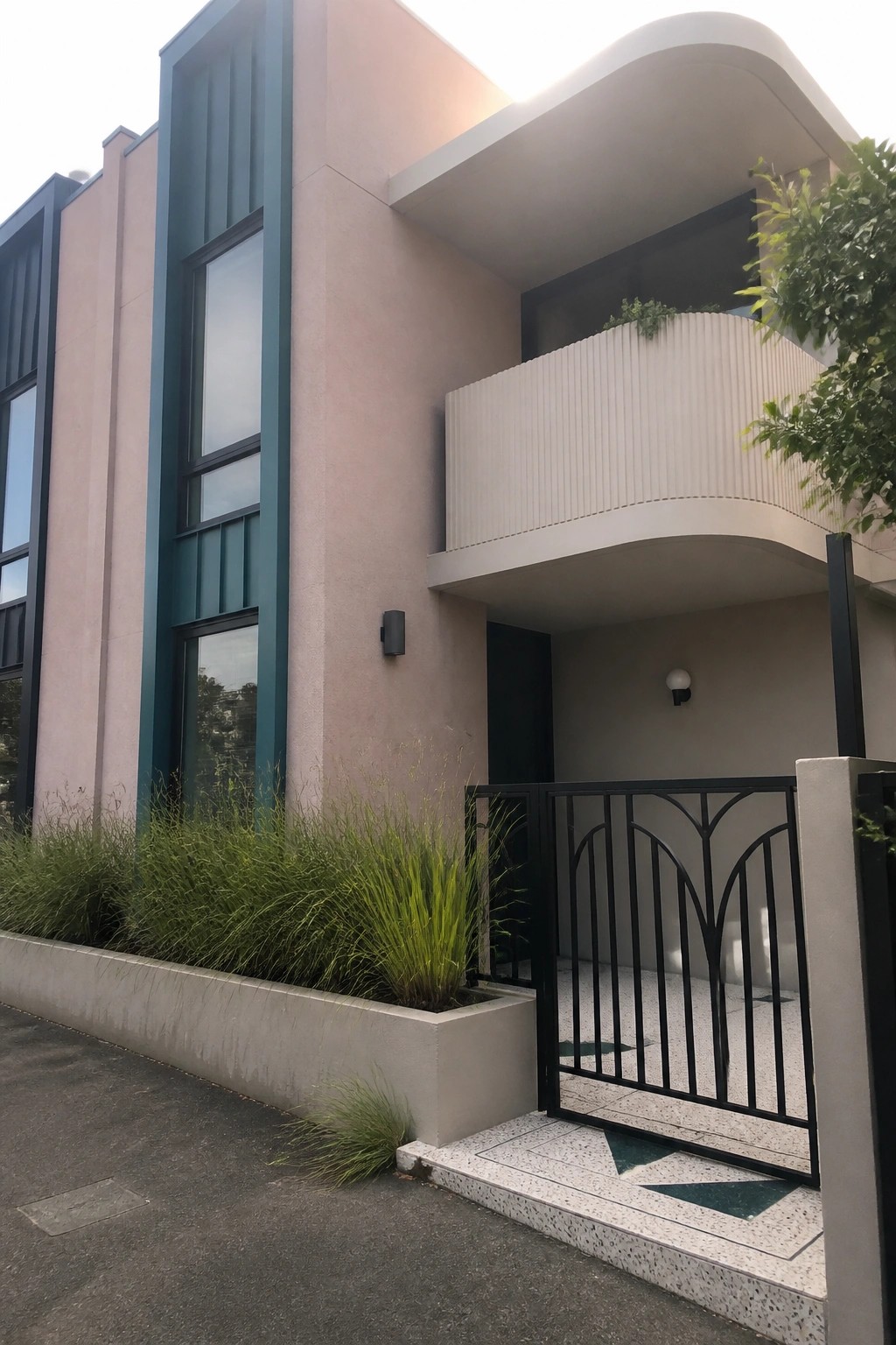 Modern pink building with teal trim, curved balcony, black metal gate, and terrazzo steps.