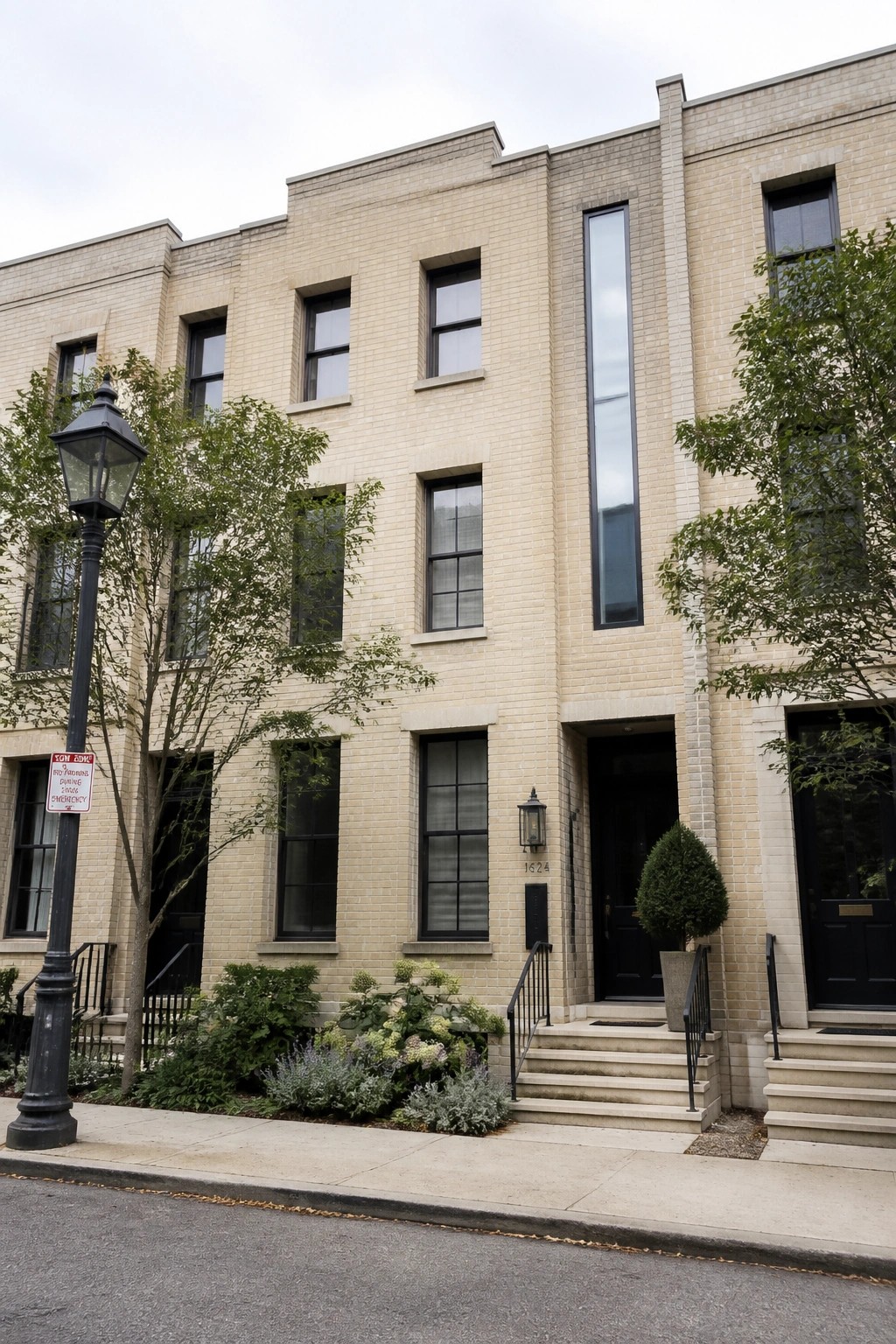Beige brick townhouses with black doors, windows, and steps along a sidewalk.