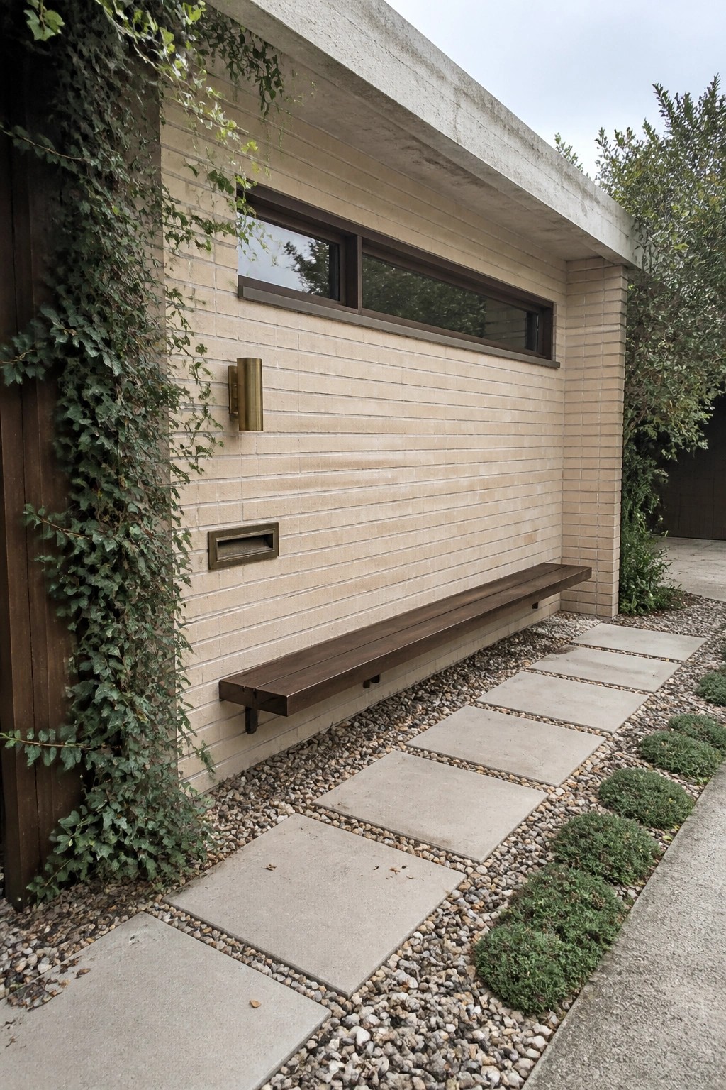 Modern brick wall with floating wooden bench, mail slot, and gravel pavers