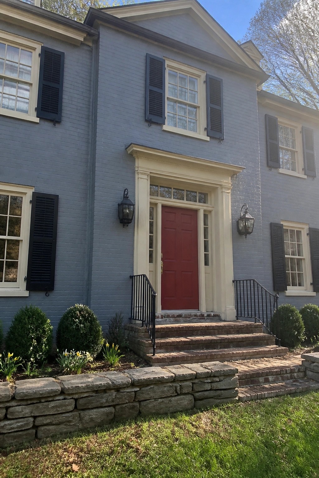 Colonial house exterior with blue gray siding, white trim, and red brick steps.