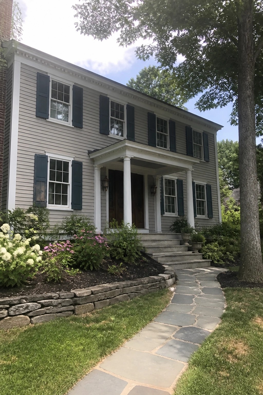Colonial house exterior with muted gray-green siding, white trim, and a stone walkway.