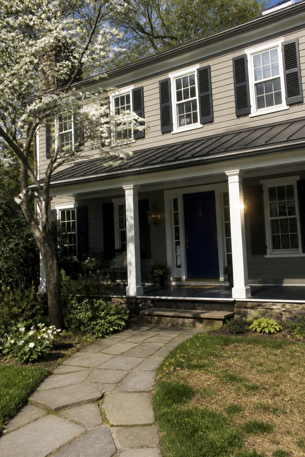 Colonial house with warm gray siding, white trim, and a stone foundation.