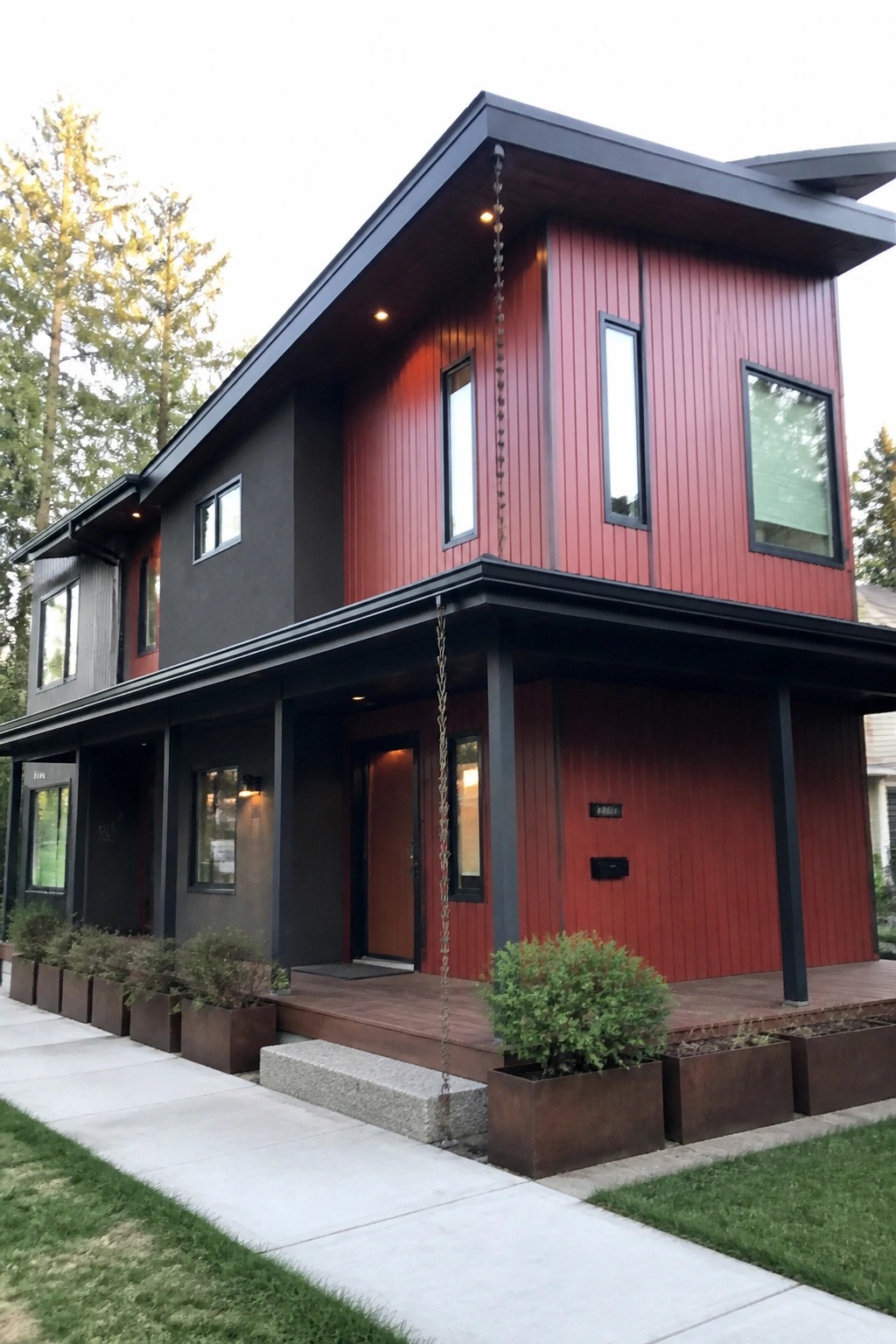 Modern two-story home with red siding, dark gray panels, wooden deck, and planters.