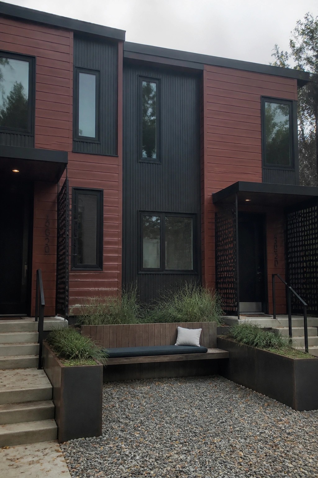 Modern two-story house exterior with red horizontal siding, black vertical panels, black windows, and two black doors with metal screens.